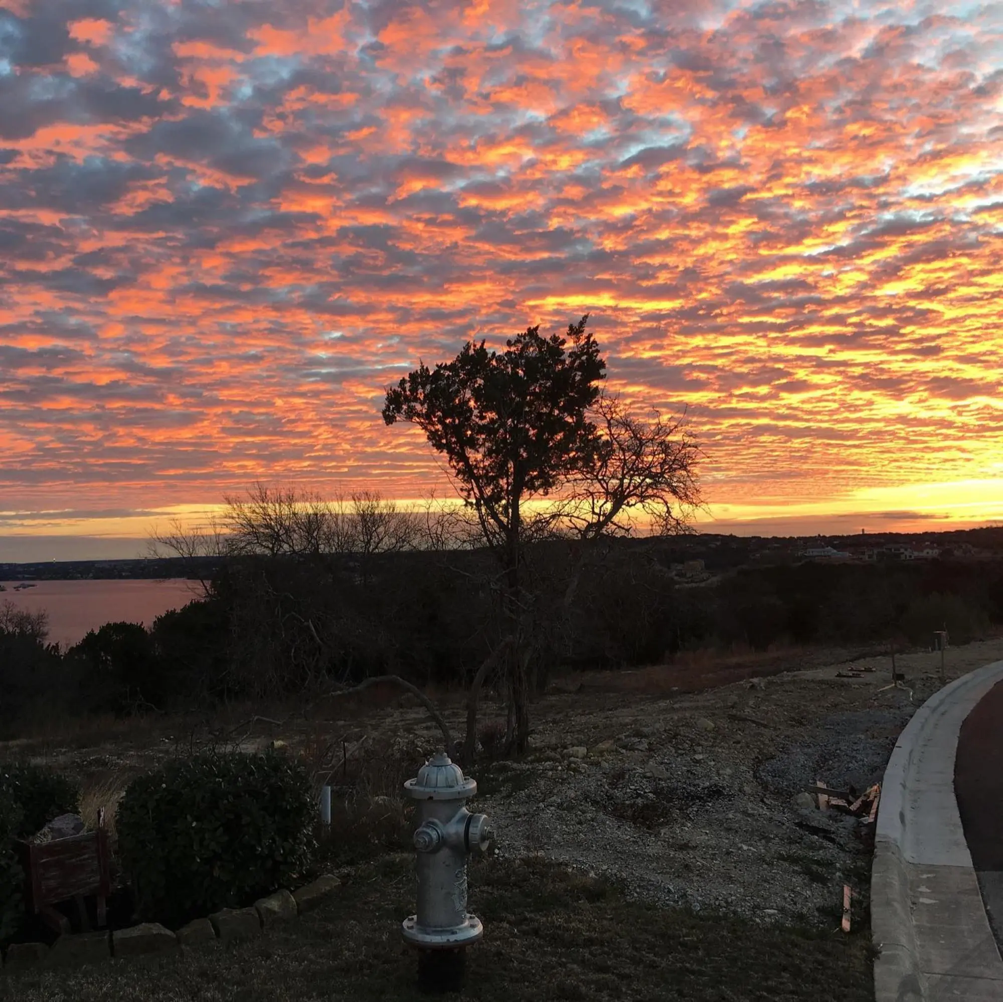 A vibrant Hill Country sunset over Lake Travis, with clouds lit up in the evening sky.